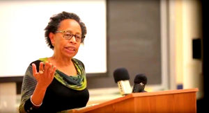 Photo of a black woman standing at a podium speaking into a microphone