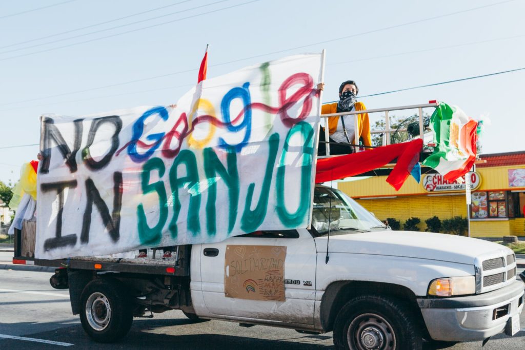 People standing in the flatbed of a white truck holding a banner that says No Google in San Jose