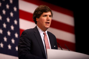 Photo of Tucker Carlson standing in front of the American flag