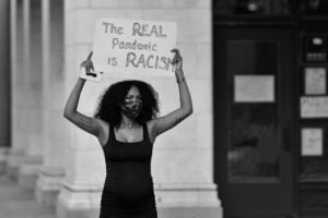 Black woman holding up a sign that says "The real pandemic is racism"