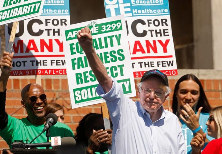 Bernie Sanders with people in the background holding up unreadable protest signs