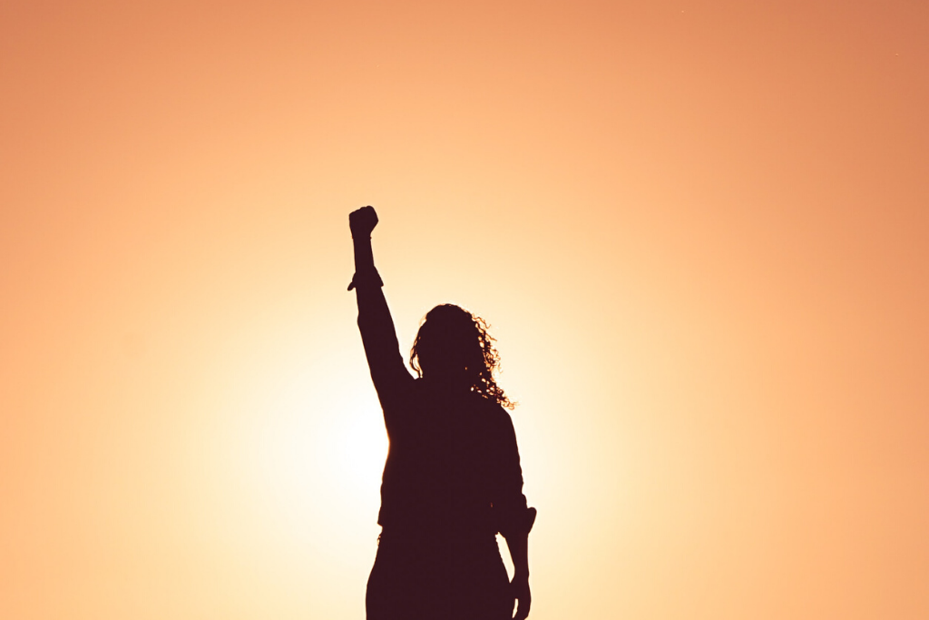 Sunset background with silhouette of a woman holding her fist in the air