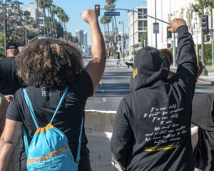 Two black people photographed from behind while marching down a street with fists in the air