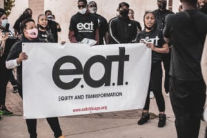 People holding up a banner that says "e.a.t. equity and transformation"