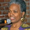 Photo of a gray haired black woman holding a microphone