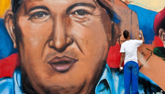 Man in a white t-shirt painting a mural featuring Hugo Chavez