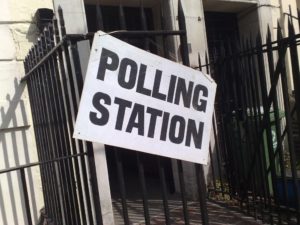 White sign on a fence that says Polling Station