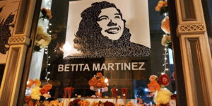 An Altar, with a portrait of Betita Martinez at the center. surrounded by flowers and lights.