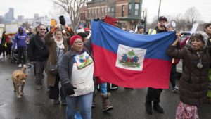 A protest march, two women leading carrying a Haitian flag.