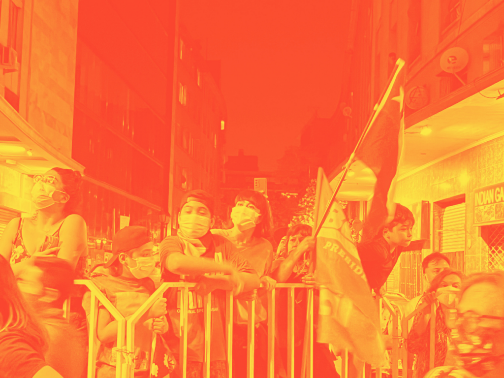 Yellow and orange tinted image showing people standing behind a metal barrier at a protest