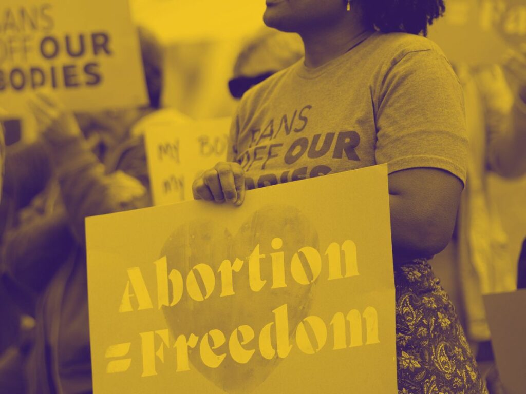 Image of a person holding a sign that reads "Abortion = Freedom" standing in a crowd of others with signs in their hands with similar messages