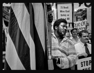Bob Gumpert photo of Harlan County miners 1974, with a Black man holding a flag in the foreground, UMWA's Harry Patrick in right corner.