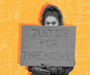 A person stands behind a sign they hold that says "JUSTICE FOR TYRE NICHOLS"