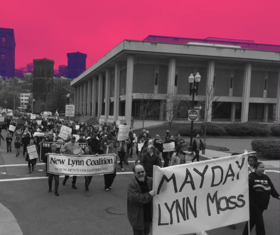 May Day, Lynn MA: Crowd of people marching behind a banner in a worn-down small city.