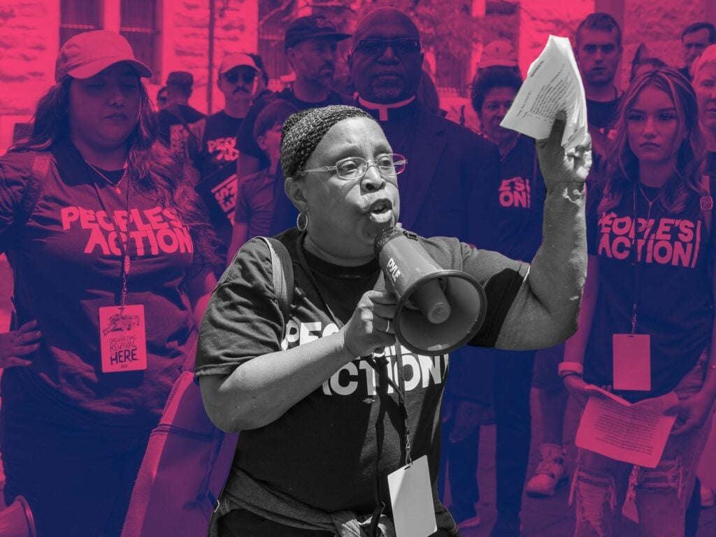 Woman leaning forward with urgency, holding a bullhorn with one hand and speaking into it, other hand brandishing papers
