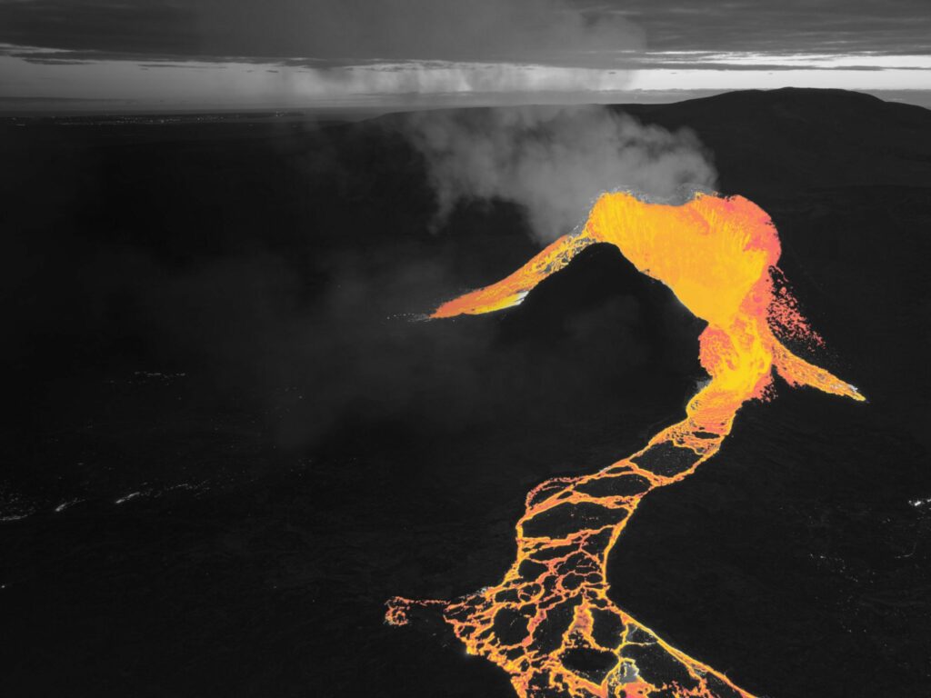 Image of an erupting volcano, a black mountain against a dark background with a bright flow of pinky orange lava.