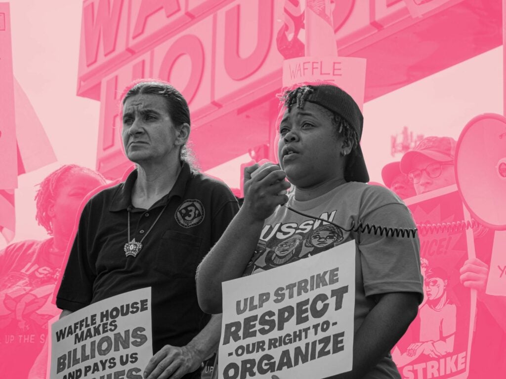A middle-aged-looking white man, hair in a pony tail, shares a stage with a young Black woman. She is speaking into a bullhorn, wearing a USSW T-shirt. They're in front of a Waffle House sign, holding placards about an unfair labor practice strike.