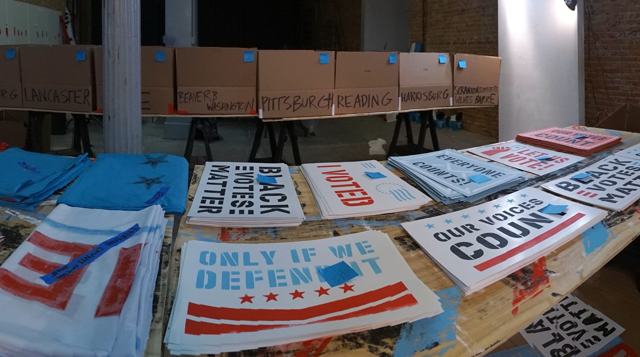 A wide-angle photo of stacks of stenciled signs and banners on a table.