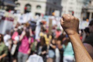 photo of a fist in air set against background of out of focus crowd in street.