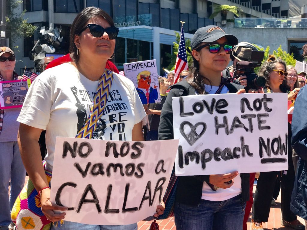 2 people holding up signs that say (sign 1) No nos vamas a callar and (sign 2) Love not hate Impeach now
