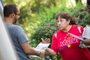 Photo of a woman wearing a red Working America tshirt talking to a man holding a flyer in his hands