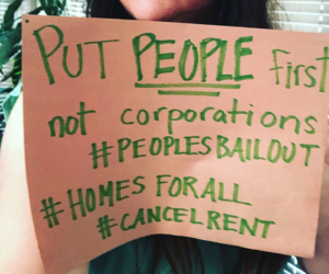 Photograph of a sign that says "Put people first not corporations #PeoplesBailout #HomesForAll #CancelRent