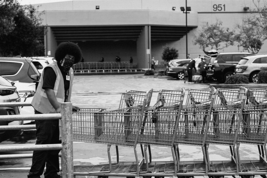 Black and white image of a grocery store worker coralling shopping carts in the parking lot