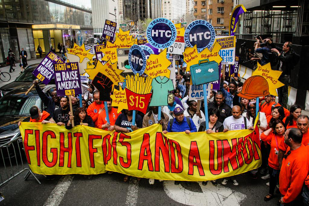 Workers marching behind a banner that says "Fight for 15 and a Union"