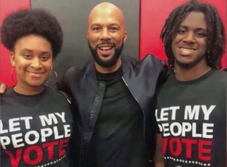 Two black women with a black man standing between them. The women are wearing tshirts that say "Let my people vote"