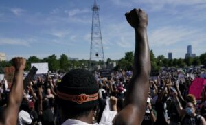 Photo with man in foreground holding up his fist to a backdrop of people at a protest