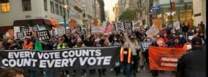 People marching behind a banner that says Count Every Vote