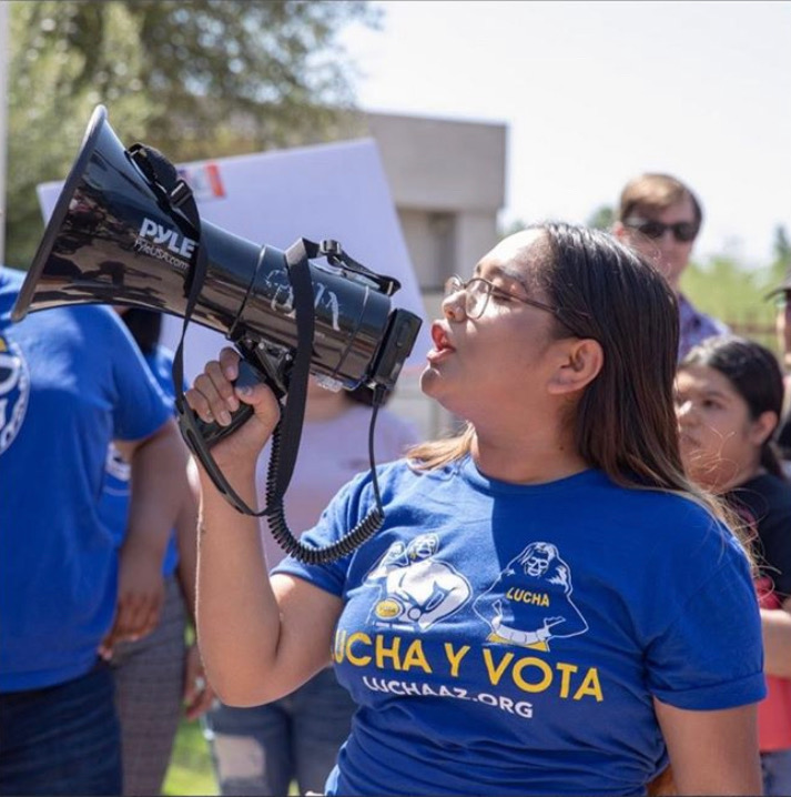Woman with long hair wearing a blue tshirt holds a megaphone to her mouth