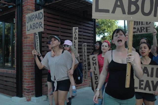 Women holding picket signs against unpaid labor at a protest