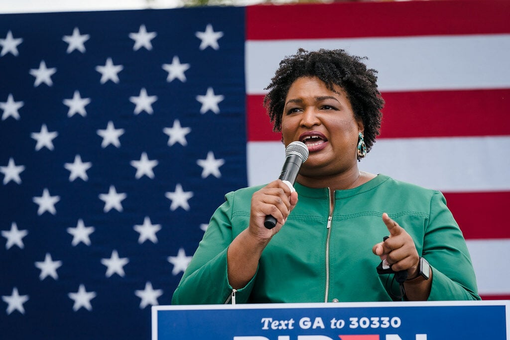 Photo of a black woman with a microphone with American flag in the background