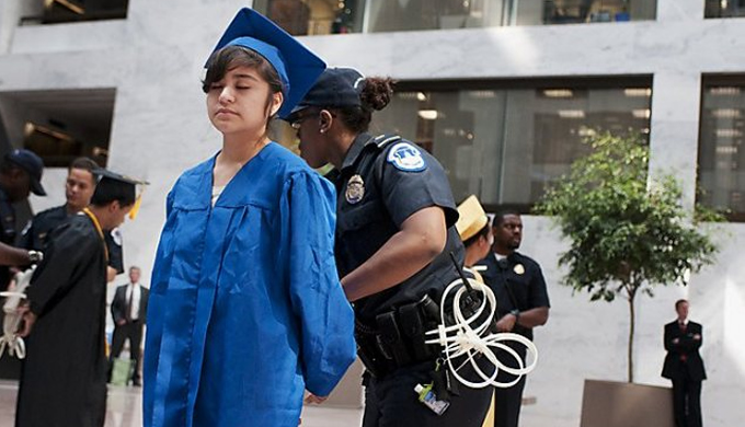 Picture of a woman in blue graduation robes being arrested