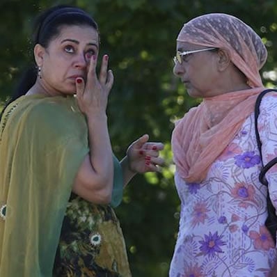 Two women standing next to each other looking sad, one is wiping tears from her eyes