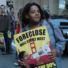 Woman holding a yellow sign that says Foreclose and underneath says Wall Street West
