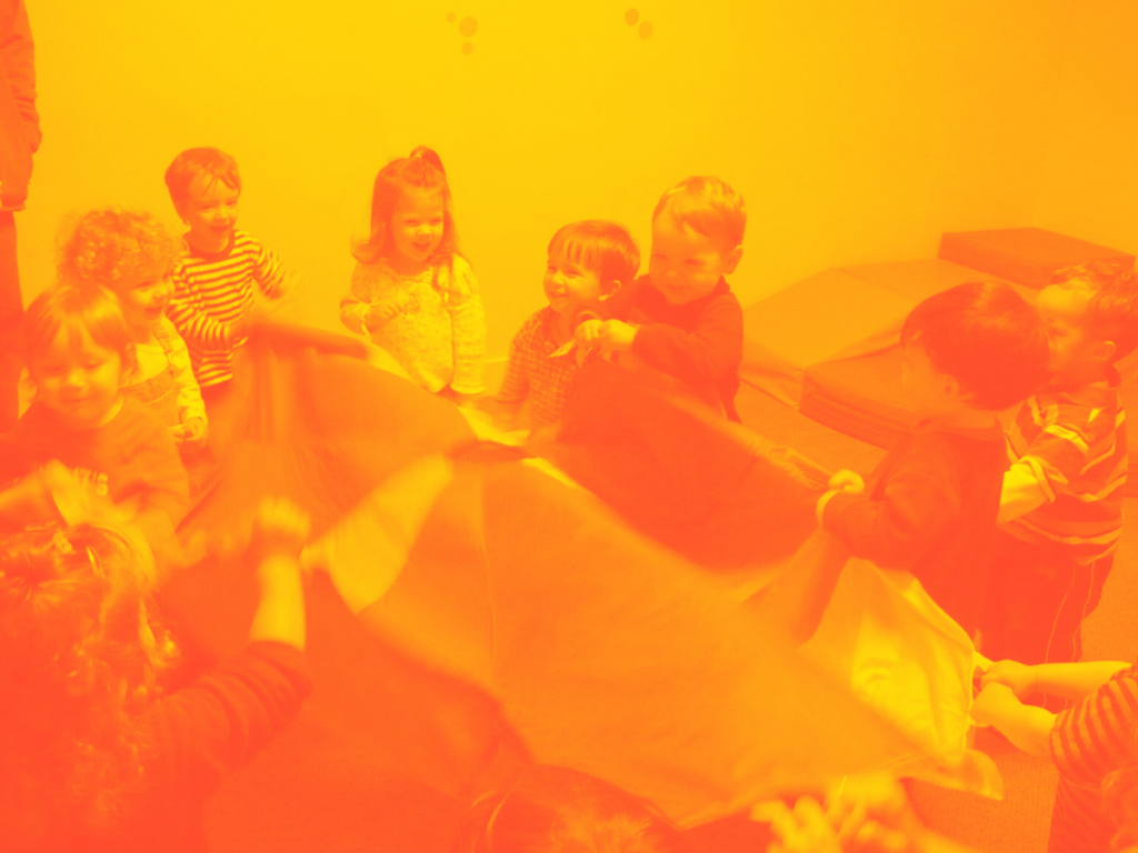 Children gathered around a piece of cloth, possibly part of an umbrella