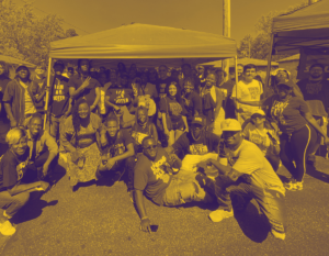 Tight group of people posed under a canopy on pavement; they're smiling, many wearing T-shirts, jeans, baseball caps. T-shirts read 'I am a Voter," "Working Families Party," Unions for All."